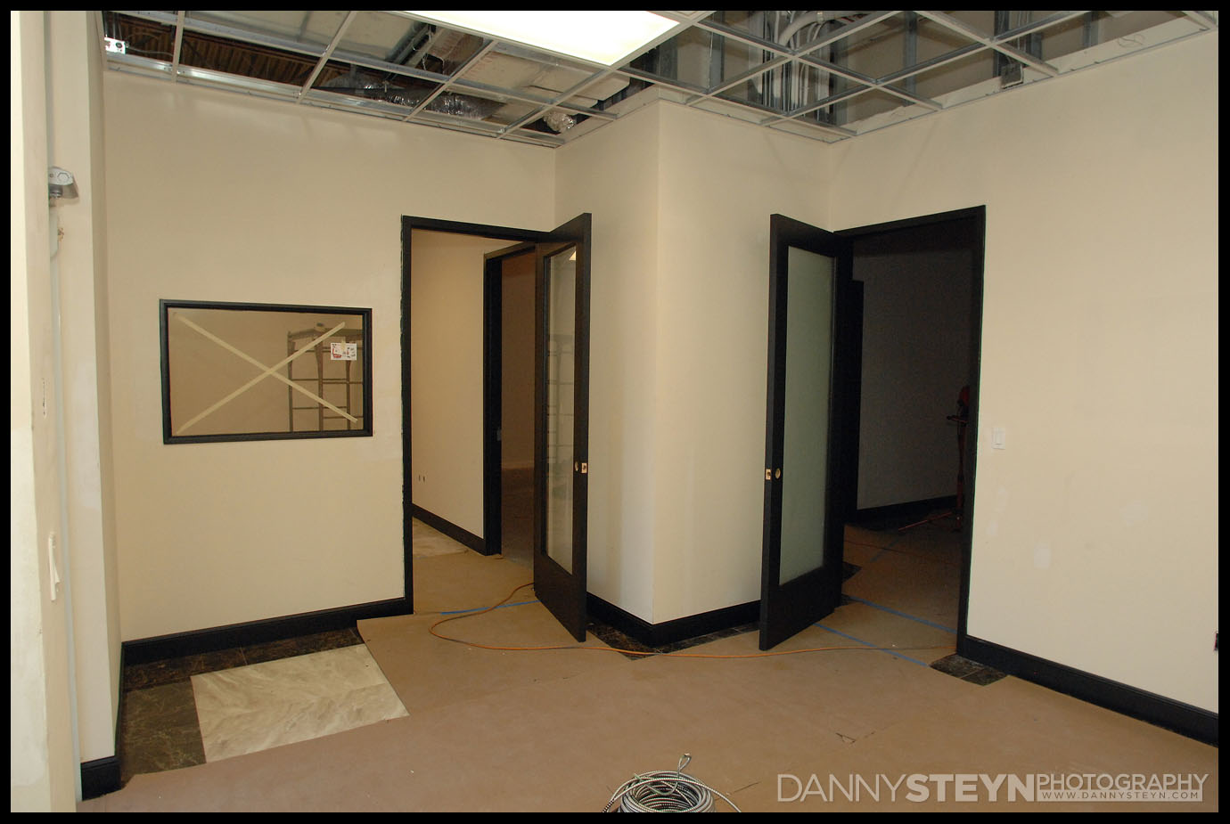 Photo Studio front Lobby showing tiles, black 8ft doors with frosted glass, and black baseboards. Lighting and drop ceiling being hung.